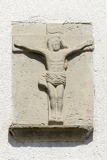 Détail du bas relief figurant au-dessus de la porte de grange : un Christ en croix.